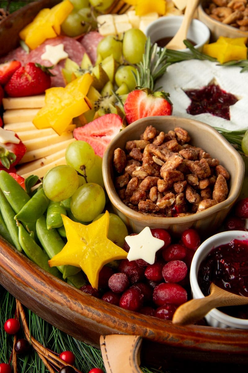 Tight view of a Christmas charcuterie tray with fresh fruits, veggies, cheeses, and nuts, some fruit and cheeses cut into star shapes.