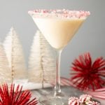A creamy martini cocktail stands in a martini glass with a crushed candy cane rim.