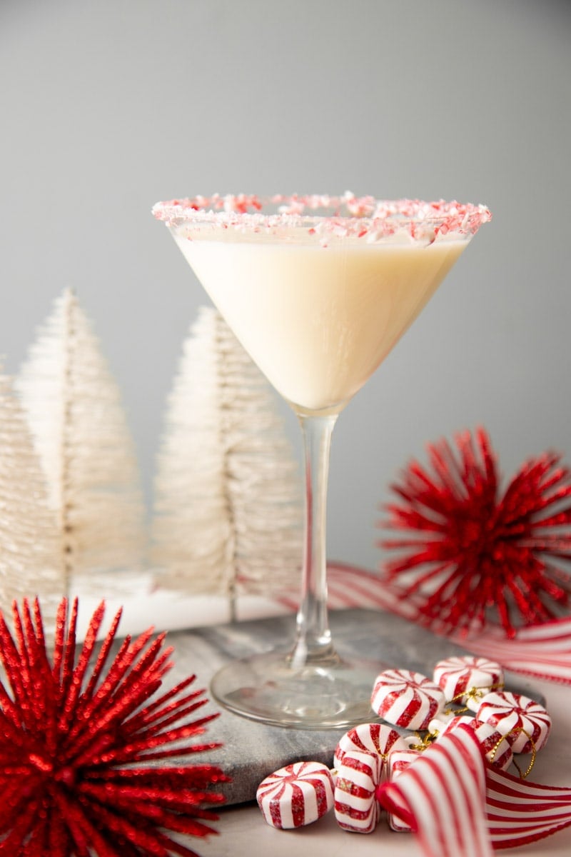 A creamy martini cocktail stands in a martini glass with a crushed candy cane rim.