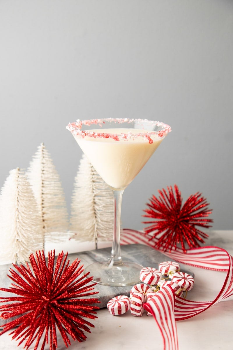 A creamy holiday cocktail stands surrounded by festive red and white decor.