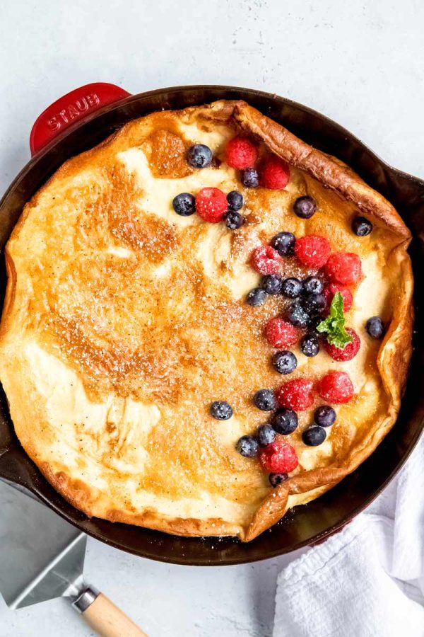 Birdseye view of a finnish pancake in an enameled cast iron skillet with fresh raspberries and blueberries along one side of it.