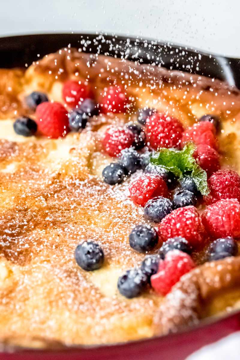 A flurry of powdered sugar dusts a warm oven pancake and the fresh berries topping it.