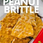 A red tin is packed with peanut candy pieces cushioned in soft white linen. A text overlay reads, "Homemade peanut brittle. Great for gifting!"