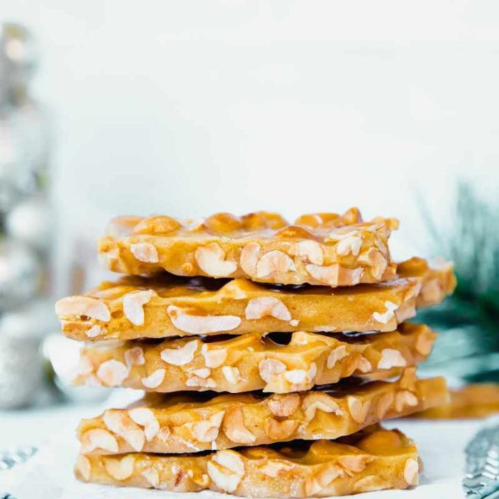 Close view of pieces of homemade peanut brittle stacked tall on a parchment paper lined cooling rack.