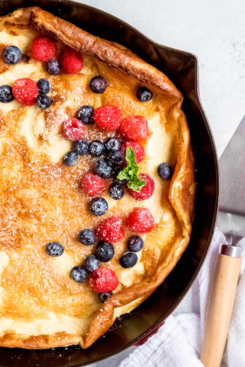 Close view of a pannukkaku topped with fresh berries and a dusting of powdered sugar in a cast iron skillet.