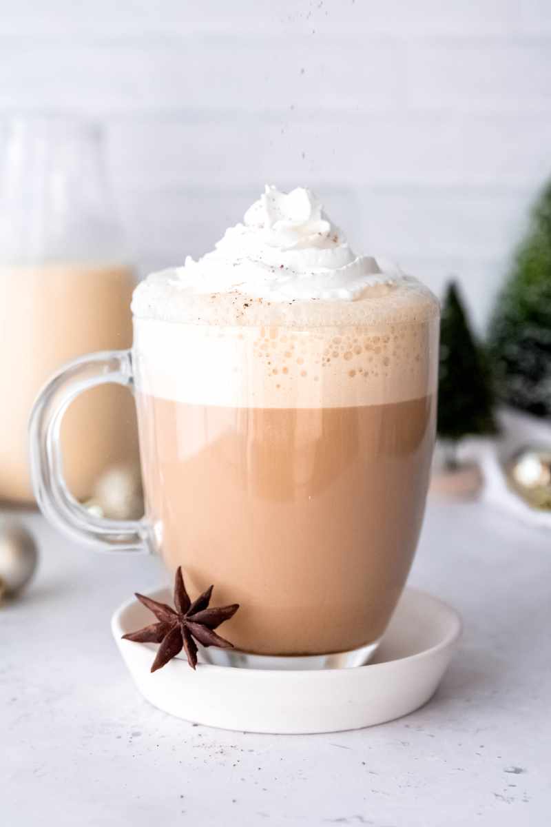 A sprinkling of nutmeg rains down over the whipped cream garnish on a festive holiday latte.