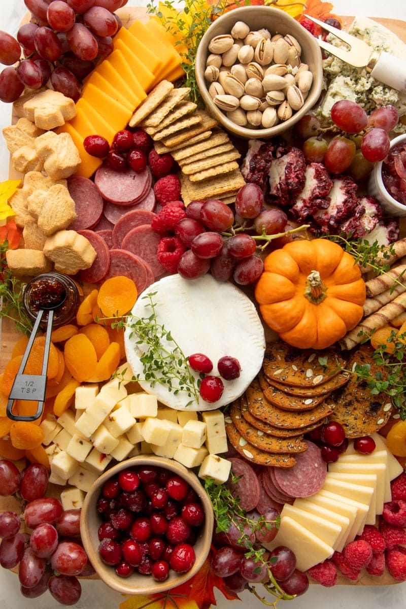 Close view of an appetizer board perfect for Thanksgiving with cheese, crackers, meats, fresh and dried fruits, and nuts.
