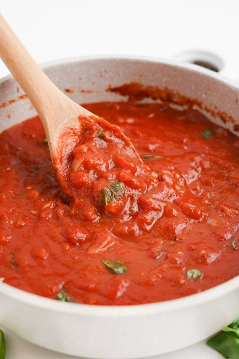 A wooden spoon lifts up a scoop of spicy arrabbiata sauce from a large bowl.