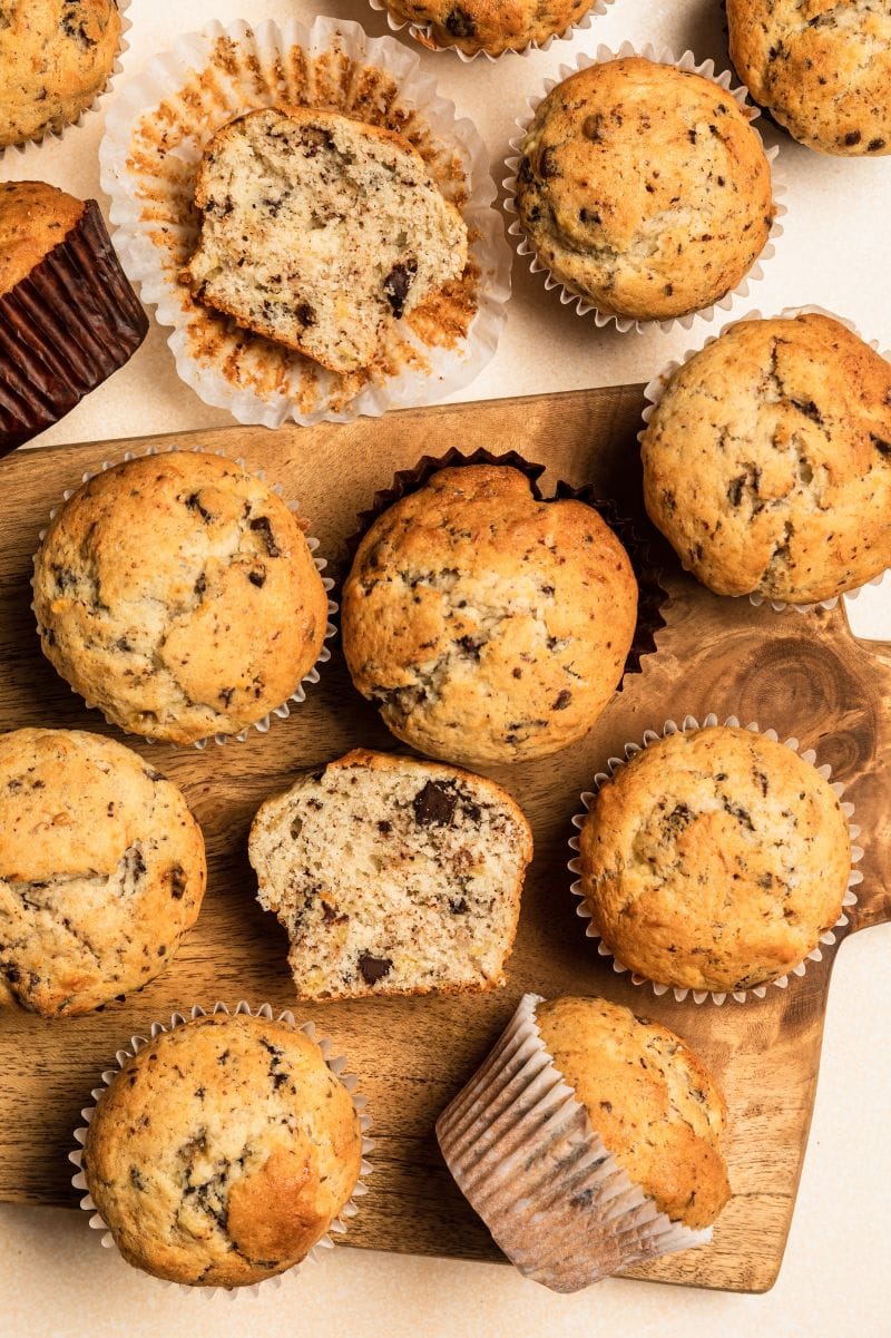 Close view of whole and cut chocolate chip banana muffins on a wooden board.