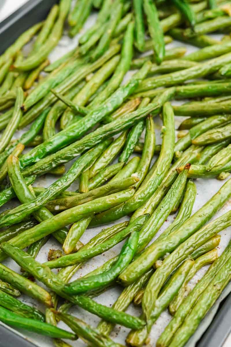 Close view of a parchment paper lined baking sheet with oven cooked green beans on it.