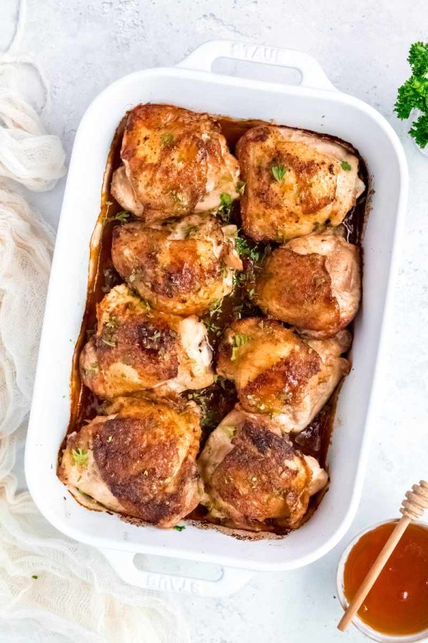 Honey garlic chicken thighs served in a white baking dish with additional honey on the side.