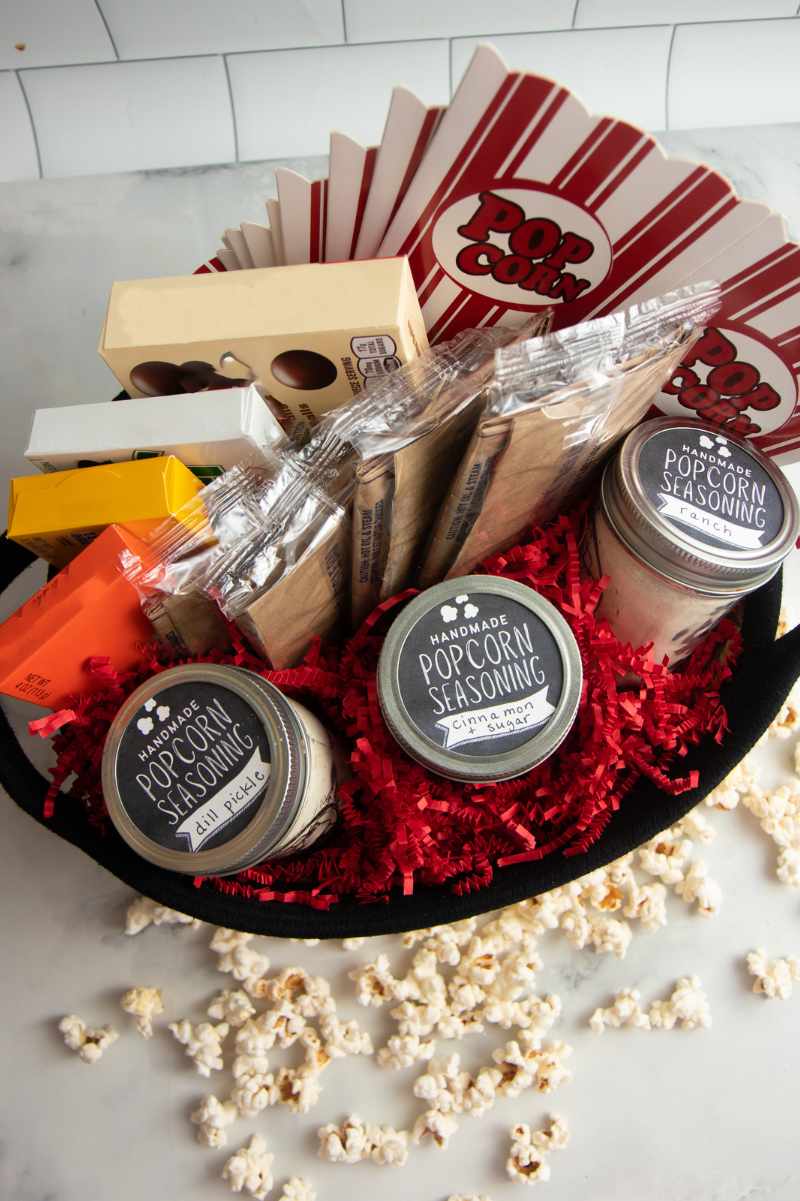 Overhead of a thoughtful movie night gift basket with classic snacks like candy and popcorn with homemade popcorn flavorings.