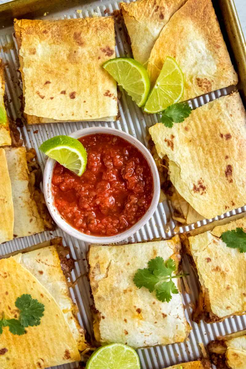Quesadilla squares and salsa served on a baking sheet, family-style.