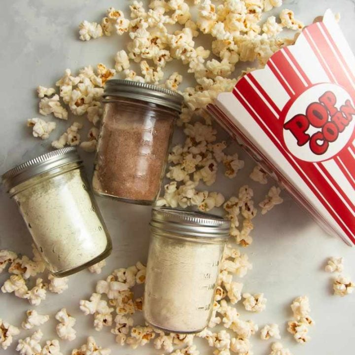 Three jars of homemade seasonings lying on their sides with popcorn spilling from a box all around them.
