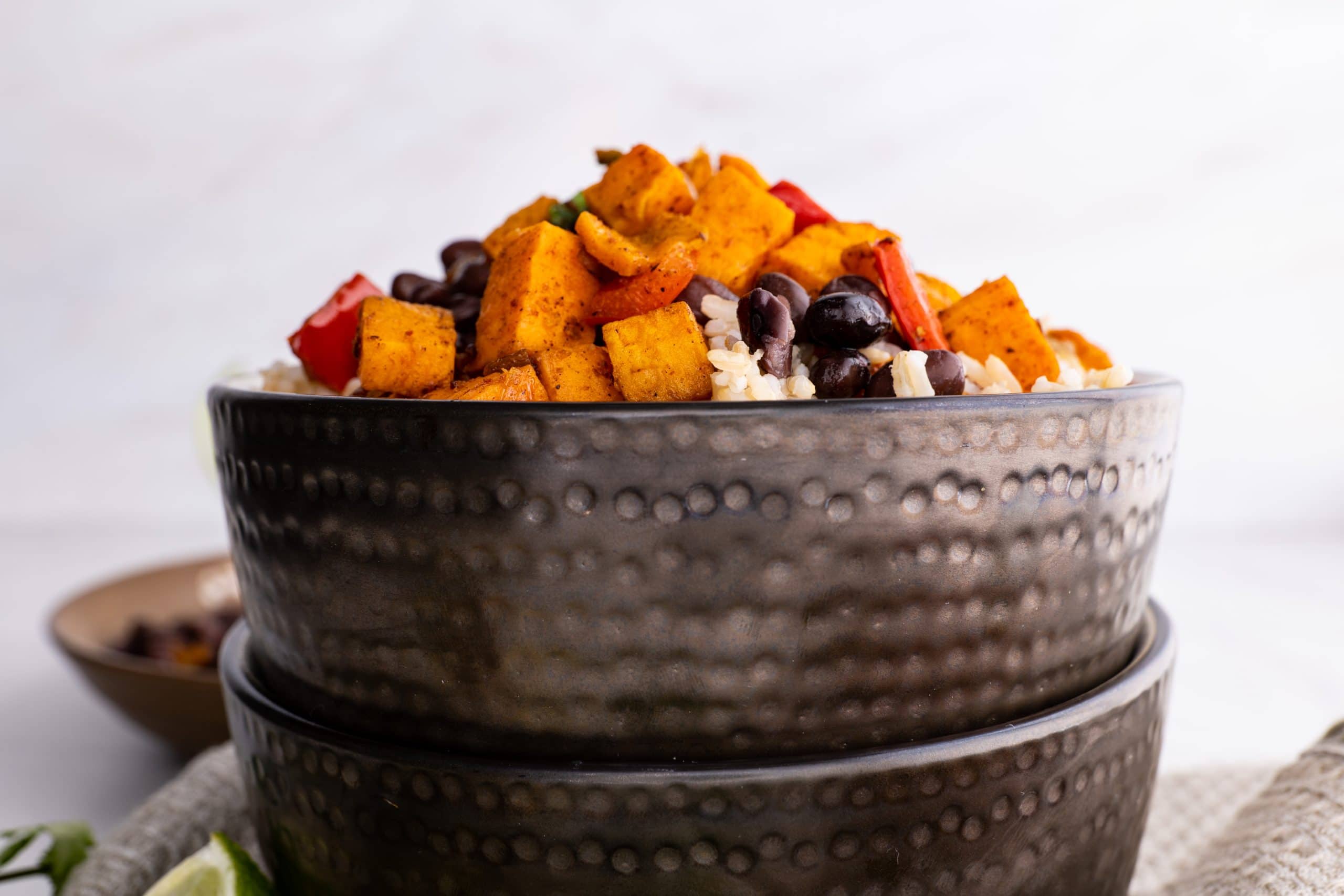 Dark textured bowl full of roasted vegetables, black beans, and rice