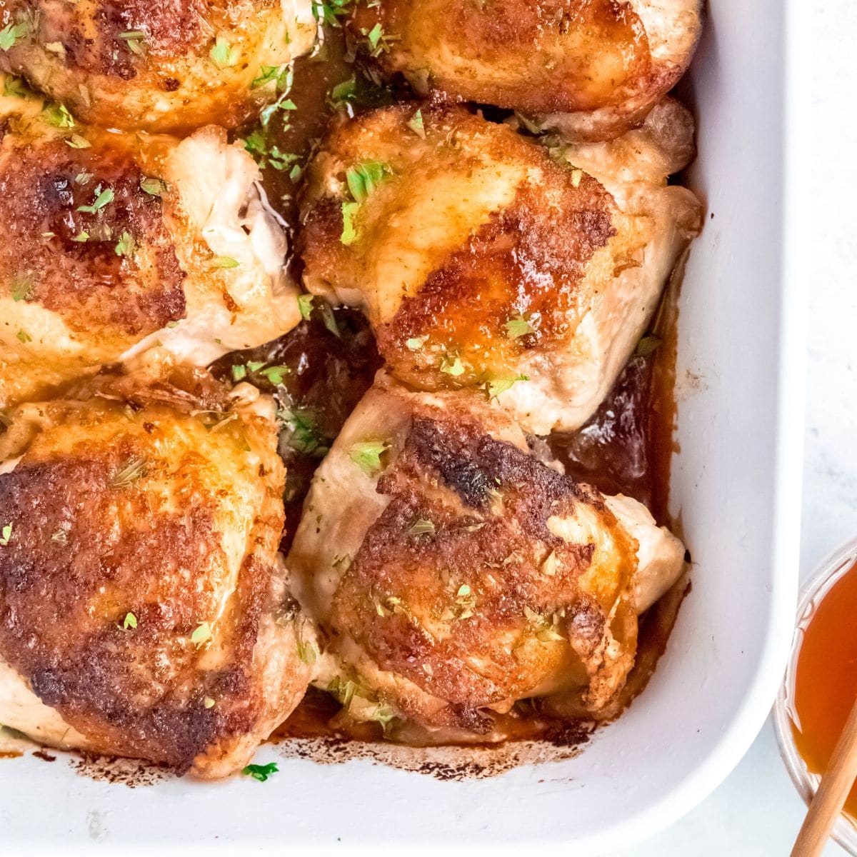 A baking dish of baked honey garlic chicken thighs, golden and glazed