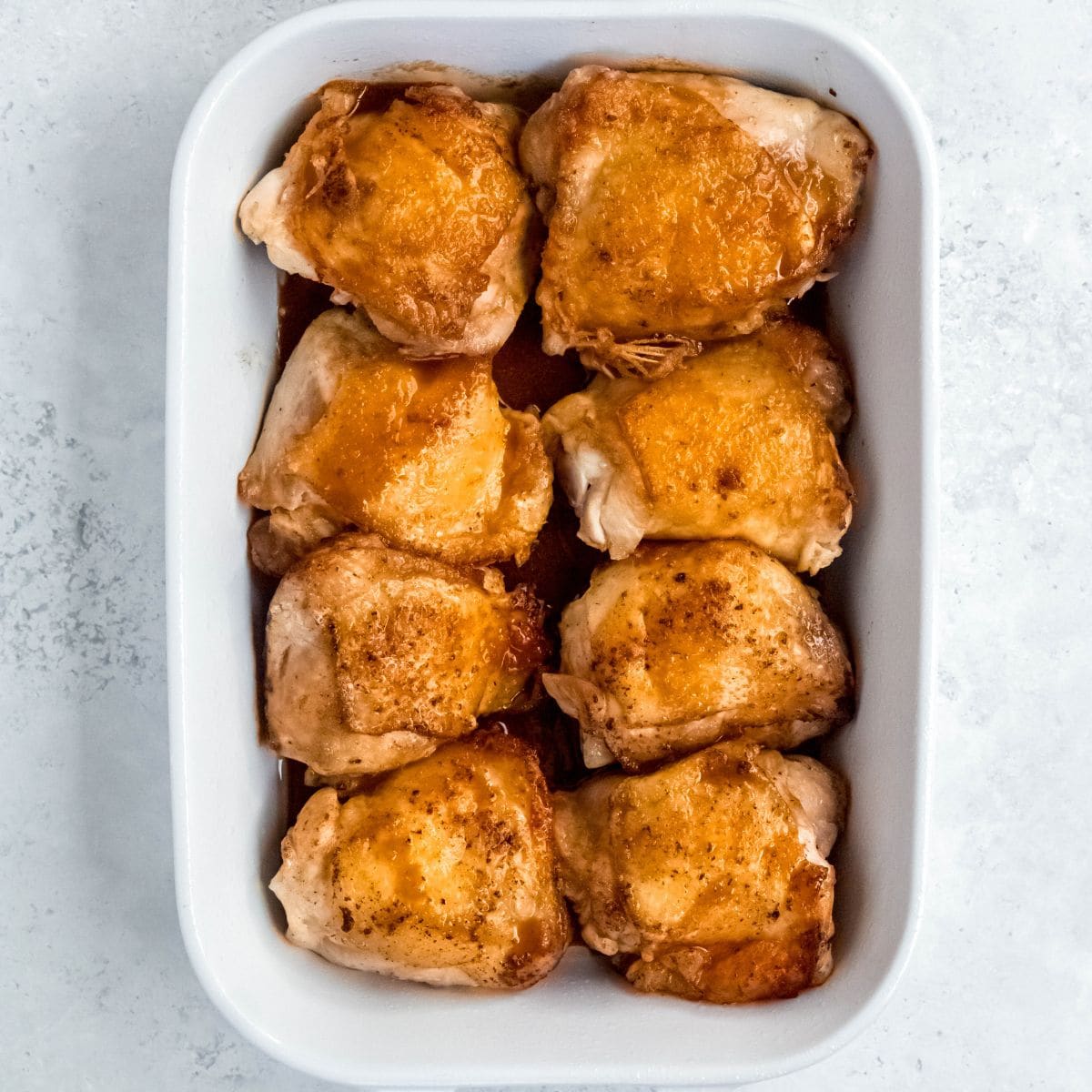 Seared chicken thighs arranged in a baking dish and coated with honey garlic sauce before baking