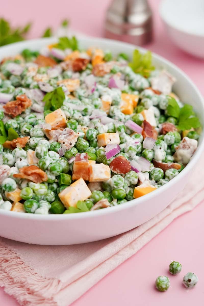 Creamy potluck salad in a white serving bowl on a pink counter with a pink kitchen linen underneath.