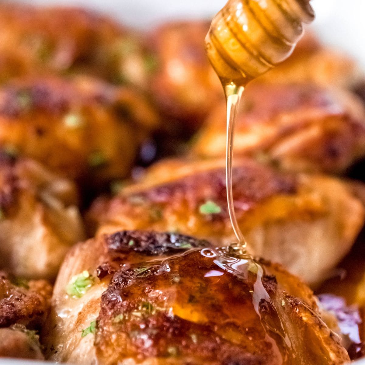 Honey being drizzled over baked chicken thighs