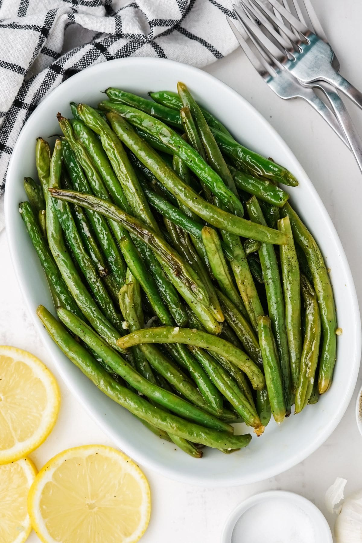 Garlic roasted green beans served on a white platter with lemon slices