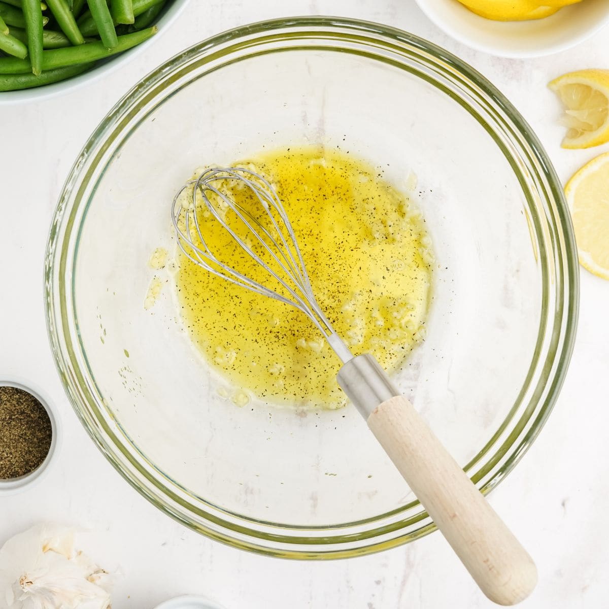 Whisk mixing olive oil, garlic, and black pepper dressing in a glass bowl