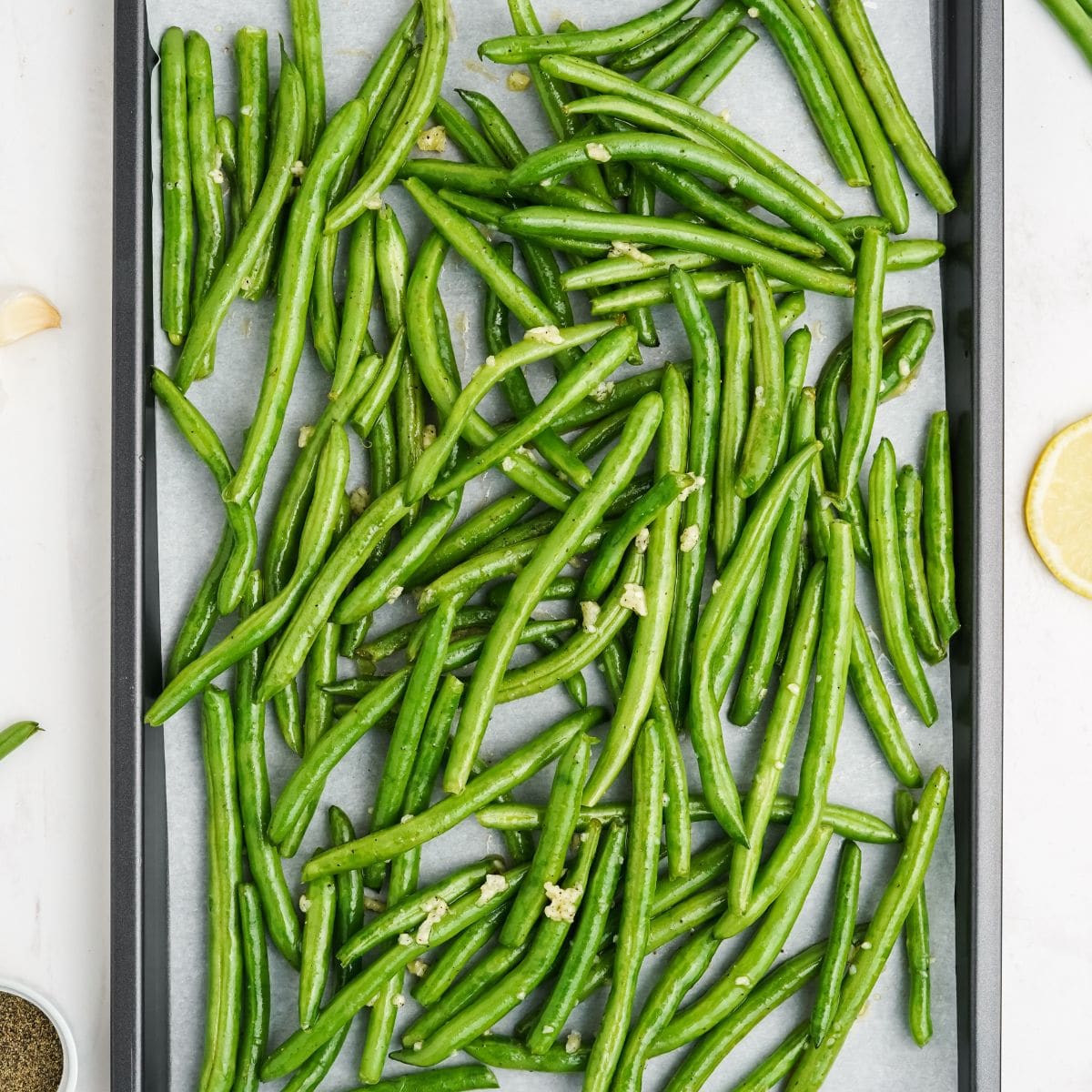 Green beans coated in garlic dressing spread on a parchment-lined baking sheet