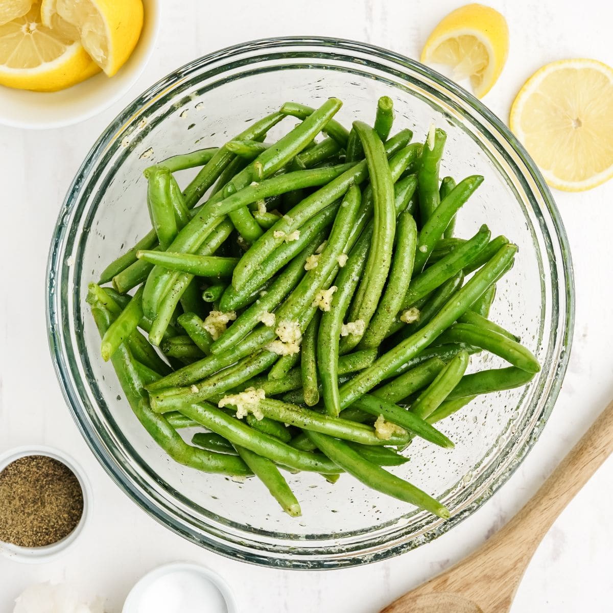 Raw green beans tossed in garlic and olive oil dressing in a glass bowl