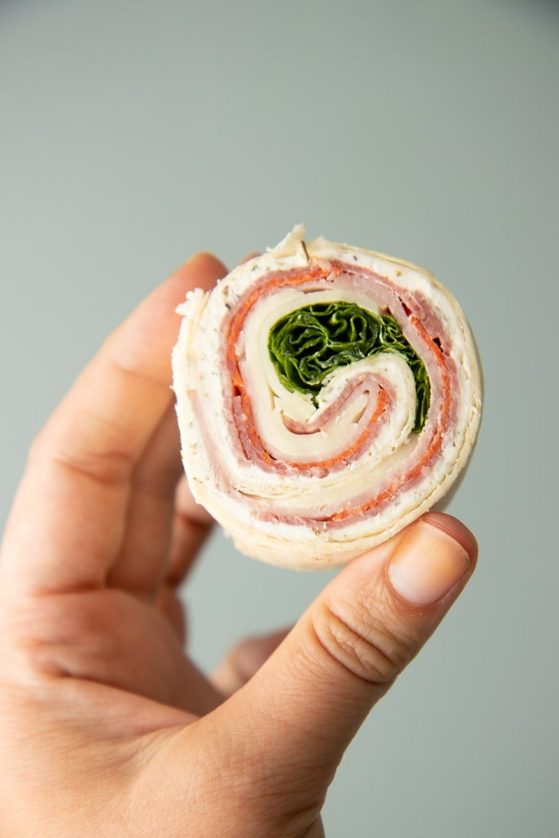 A hand holds up an italian pinwheel on a light background.