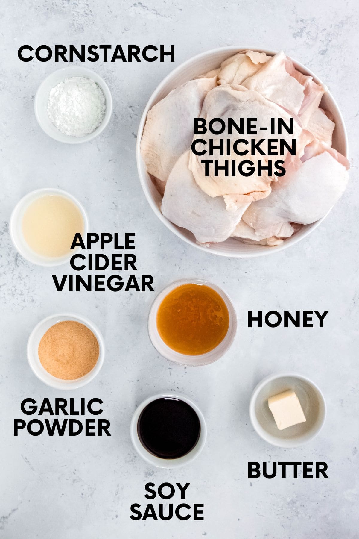 Labeled ingredients for honey garlic chicken thighs, including bone-in chicken thighs, honey, soy sauce, apple cider vinegar, garlic powder, cornstarch, and butter