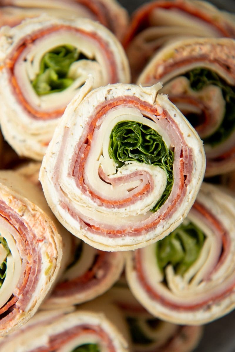 Close view of an italian pinwheel showing the meat, cheese, and lettuce fillings in a spiral.