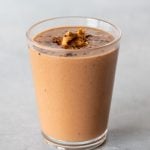 A peanut butter smoothie topped with a scoop of peanut butter and a sprinkling of cocoa powder in a glass on a light background.