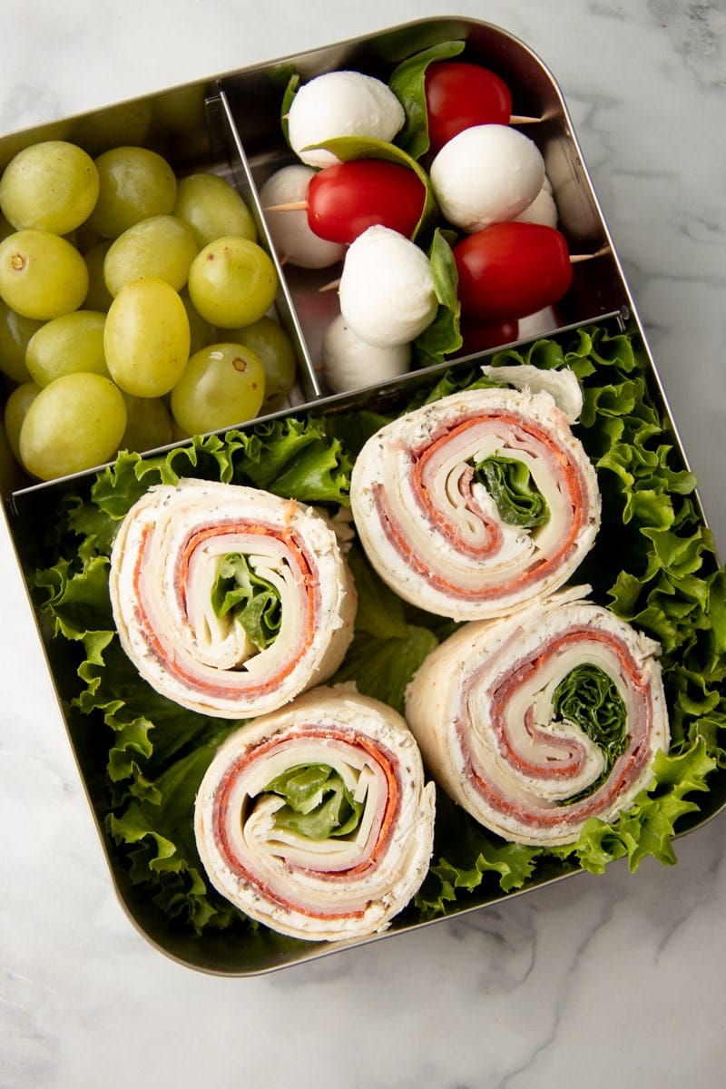 Pinwheels packed in a lunch with lettuce, grapes, and caprese sticks.
