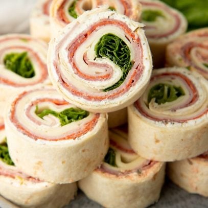 Serving platter of pinwheel appetizers stacked with one on top showing all the spiraled layers inside.