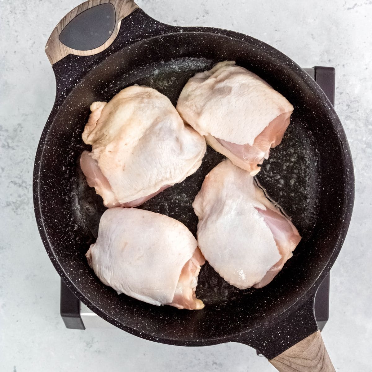 Raw chicken thighs skin-side up in a skillet before searing