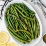 Roasted green beans with garlic and lemon on a white oval platter