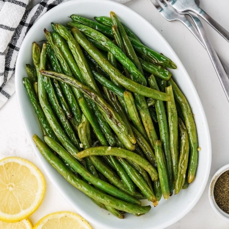 Roasted green beans with garlic and lemon on a white oval platter