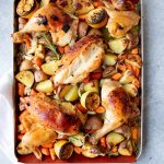 Overhead of a sheet pan loaded with roasted root veggies topped with roast chicken pieces and lemon halves.