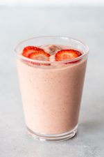 A strawberry shortcake smoothie topped with thin slices of strawberry in a glass on a light background.