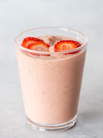 A strawberry shortcake smoothie topped with thin slices of strawberry in a glass on a light background.