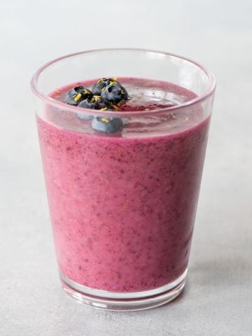 Top view of a blueberry smoothie topped with fresh berries and lemon zest.