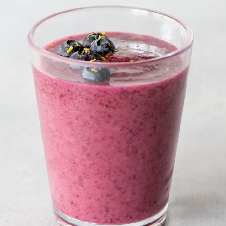 Top view of a blueberry smoothie topped with fresh berries and lemon zest.