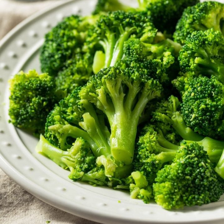 Steamed garlic broccoli served on a white plate with a linen tablecloth beneath.