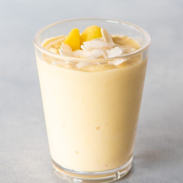 Top view of a mango smoothie topped with coconut flakes and mango pieces in a tall glass.