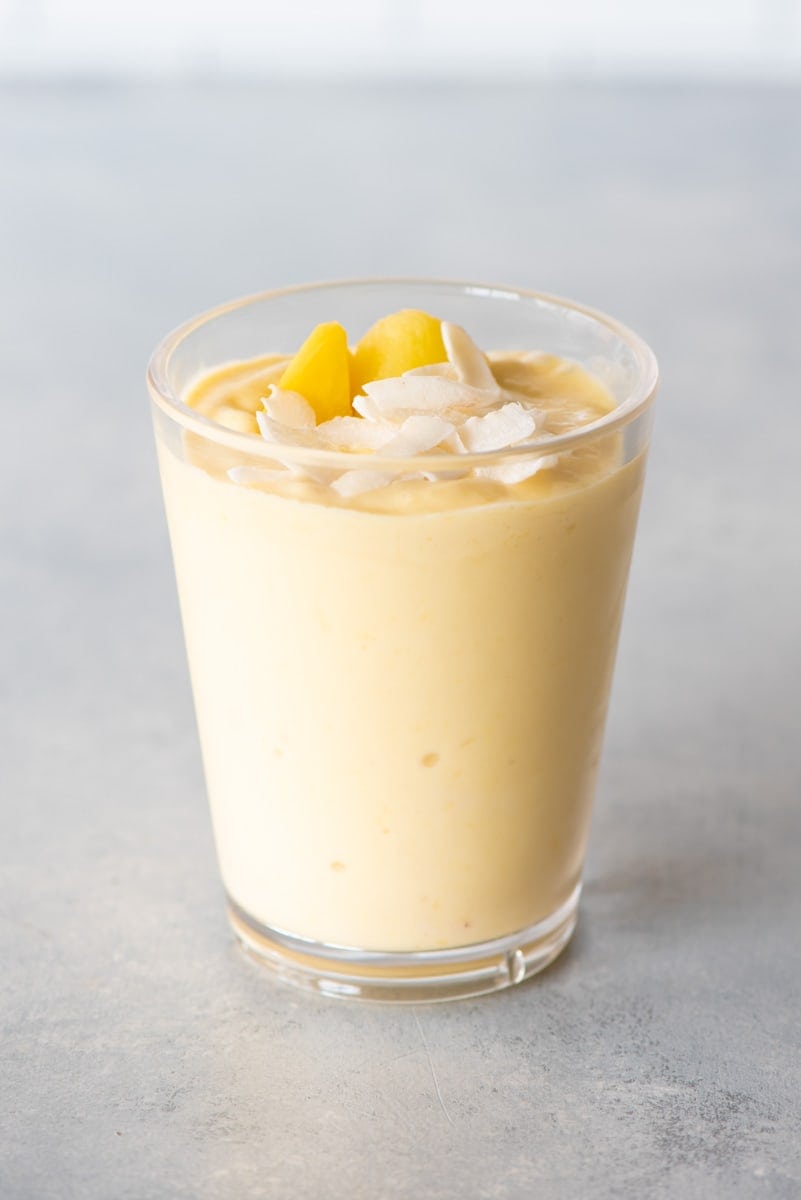 Top view of a mango smoothie topped with coconut flakes and mango pieces in a tall glass.