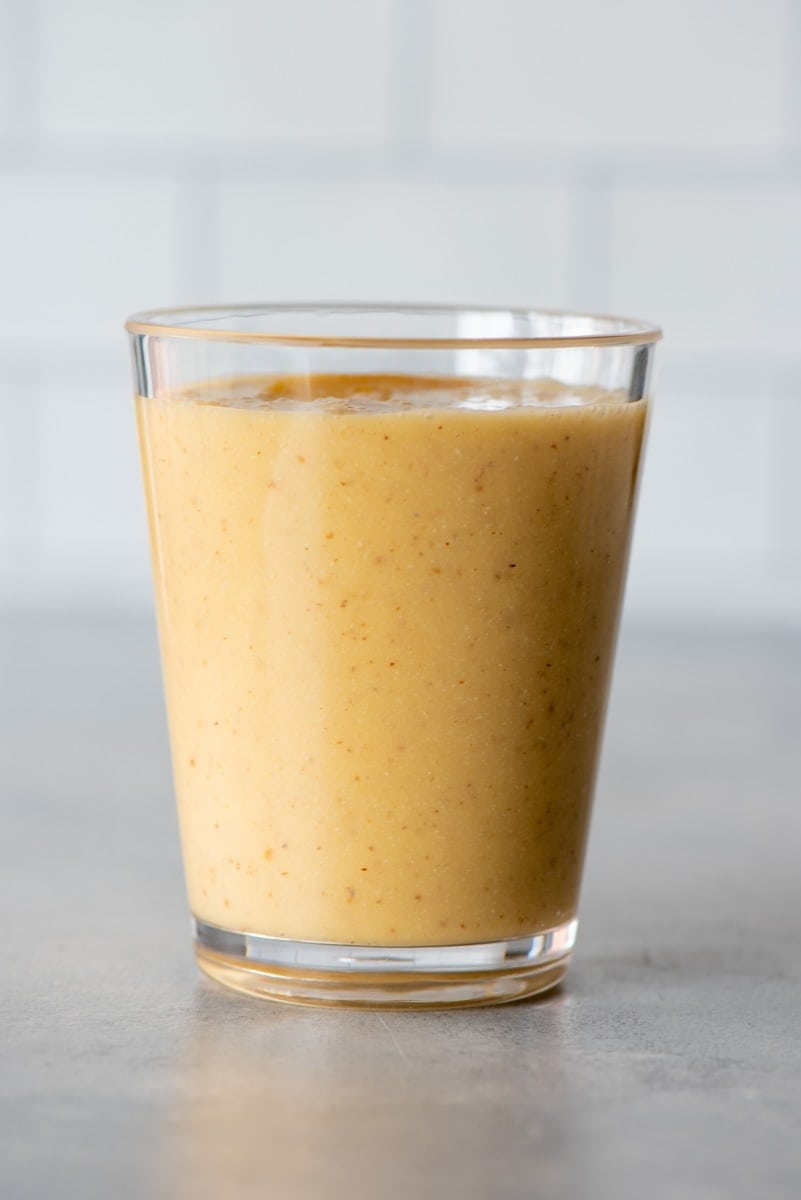 Side view of a blended frozen peach and almond drink in a glass on a light background.