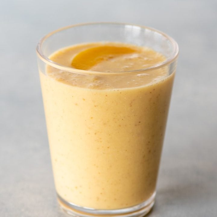 Top view of a peach smoothie in a glass with a peach slice on top.