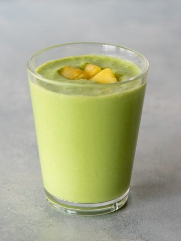 Top view of a pineapple spinach smoothie in a glass with pineapple pieces on top.
