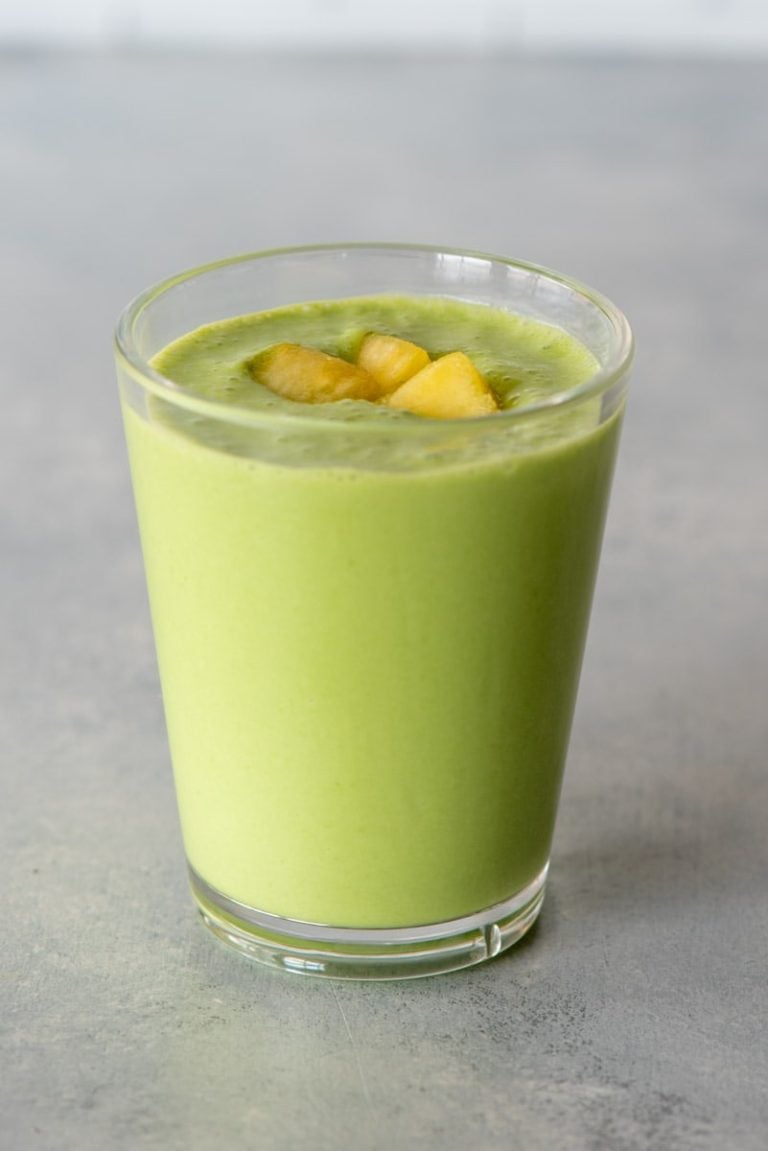 Top view of a pineapple spinach smoothie in a glass with pineapple pieces on top.