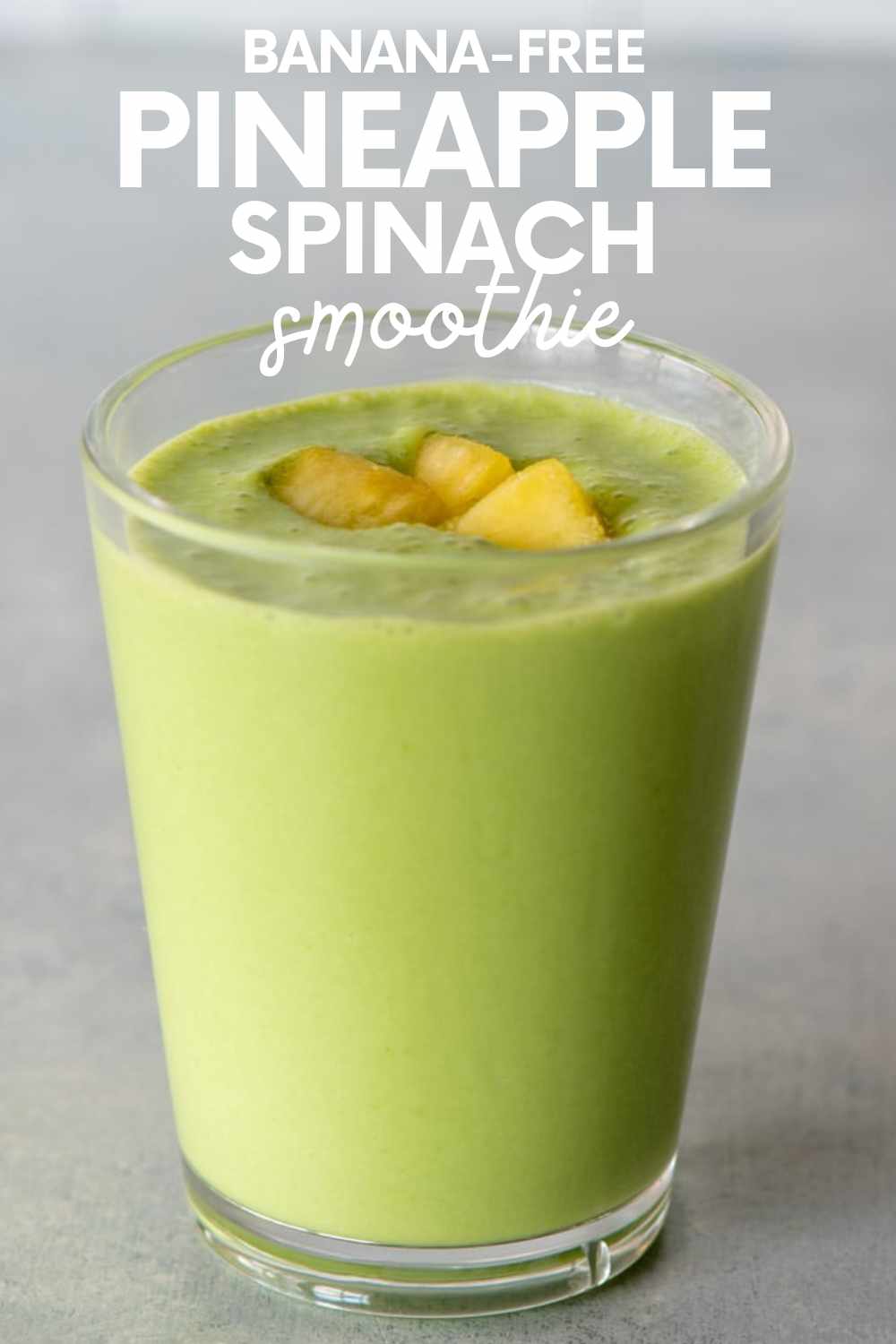 Top view of a pineapple spinach smoothie in a glass with pineapple pieces on top. A text overlay reads, "Banana-Free Pineapple Spinach Smoothie."