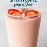 A strawberry shortcake smoothie topped with thin slices of strawberry in a glass on a light background. A text overlay reads, "Banana-Free Strawberry Shortcake Smoothie."